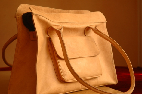 Tan leather tote bag with dual handles and front pocket, displayed against warm brown background