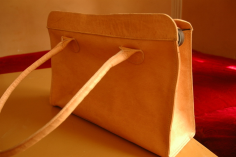 Tan leather crossbody bag with woven strap, angled view showing structured rectangular shape and rich caramel patina