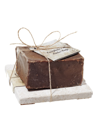 Savon artisanal marron foncé enveloppé de papier kraft, attaché avec une ficelle naturelle, posé sur un socle blanc
