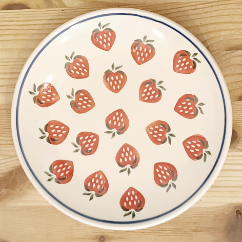 Cream ceramic plate with red strawberry pattern scattered across surface, viewed from above on wooden background