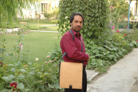 Artisan in maroon shirt holding handwoven natural textile basket outdoors in garden setting