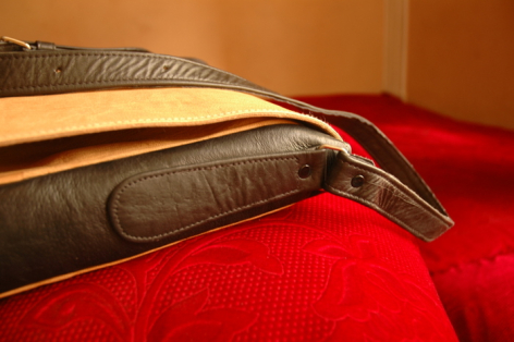 Stack of three leather belts in black, tan, and burgundy displayed at angles on red fabric background