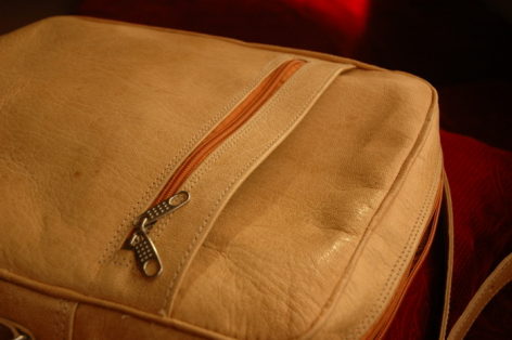 Tan leather bag with dual zippered compartments, angled front view showing textured suede surface and metal hardware