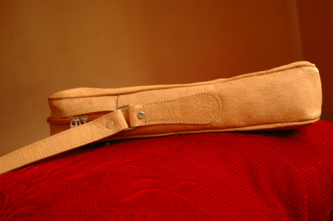 Tan leather cylindrical case with wooden toggle closure, displayed on red fabric against warm brown background