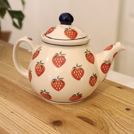 Cream ceramic teapot with red strawberry pattern and black knob on lid, front view