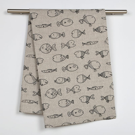 Beige linen textile with black hand-drawn fish and botanical motifs draped over a wooden rod, displayed flat lay style