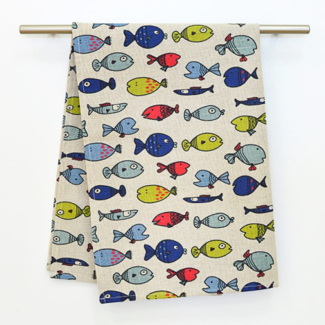 Cream linen tea towel with colorful hand-printed fish pattern in blue, yellow and red, displayed on wooden rod