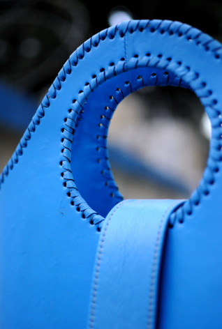 Blue leather bag detail showing decorative beaded edge stitching and circular opening, close-up view