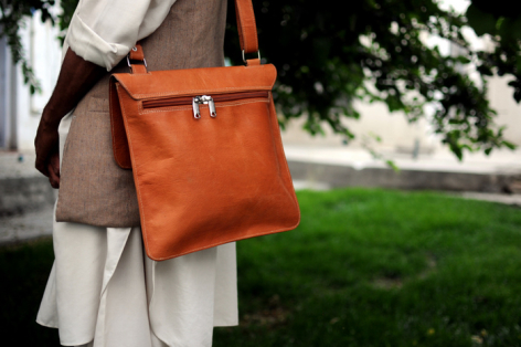Sac à main en cuir orange porté à l'épaule, vue de face en extérieur avec feuillage vert en arrière-plan