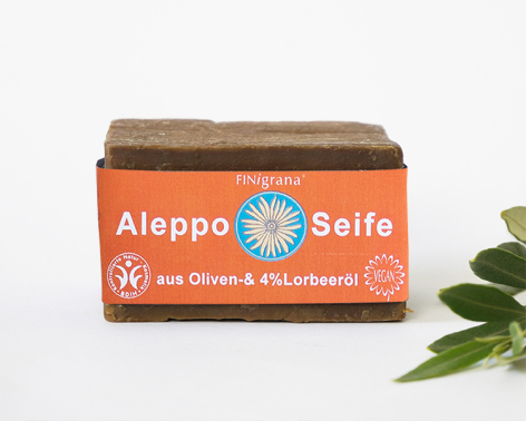 Orange Seifenbox mit traditionellem Design und weißem Text, daneben grüne Pflanze auf hellem Hintergrund