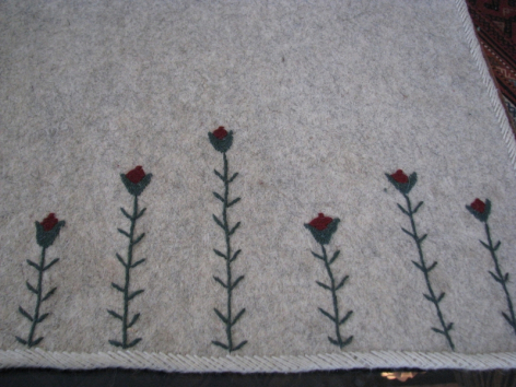 Embroidered textile detail showing six small purple flowers with green stems arranged in a row on cream-colored fabric