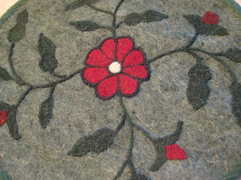 Grauer Wollstoff mit roten und grünen Blüten- und Blattmustern, Detailaufnahme der handgestickten Verzierungen