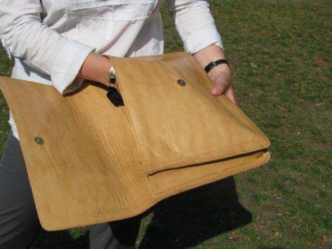 Handwerkerin hält eine hölzerne Tasche mit hellem Holzton und sichtbaren Verarbeitungslöchern in Händen, Draufsicht