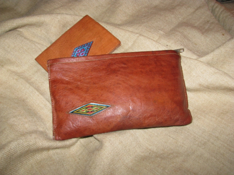 Rote Ledertasche mit silbernem Emblem, daneben blaue kleinere Tasche auf Stoffuntergrund, Draufsicht