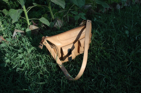 Hellbraune Ledertasche mit geometrischem Design, von oben auf grünem Moos fotografiert
