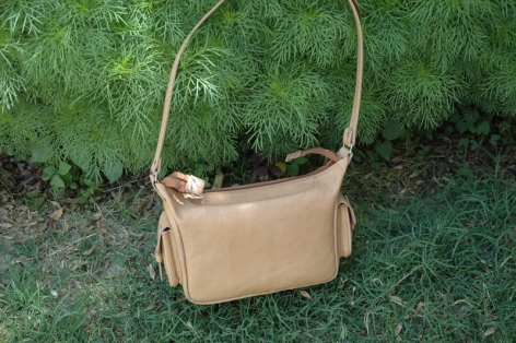 Beige Ledertasche mit Henkel, Vorderansicht auf grünem Hintergrund
