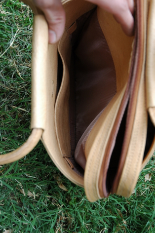 Braune Ledertasche Draufsicht mit offener Klappe und hellem Lederhenkel auf grünem Untergrund