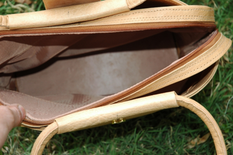Hellbraune Ledertasche von oben, offen mit dunklem Innenfutter und Trageriemen auf grünem Untergrund