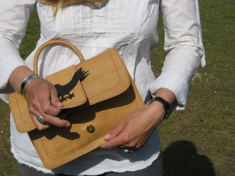 Hellbraune Ledertasche mit schwarzem Riemen wird von Person in weißem Hemd gehalten, Ansicht von oben