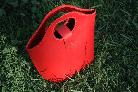 Rote Ledertasche von oben fotografiert mit charakteristischem Henkel und herzförmigem Verschluss auf grünem Untergrund