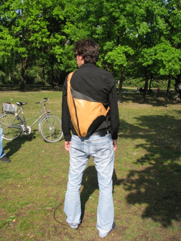 Person von hinten trägt braune Ledertasche über der Schulter, grüner Park im Hintergrund