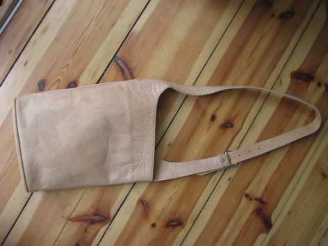 Hellbraune Ledertasche mit Schultergurt, Draufsicht auf Holzuntergrund, handwerklich gefertigte Konstruktion