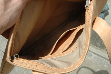 Beige Ledertasche von oben geöffnet, Innenansicht mit braunem Futter und Griffen sichtbar