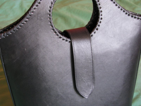 Schwarze Ledertasche mit halbmondförmiger Öffnung und geflochtener Kantenbearbeitung, Detail des Tragegriffs