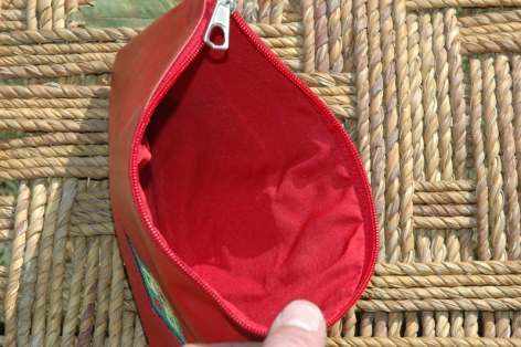 Petit sac en cuir rouge vif ouvert, révélant l'intérieur rose vif, posé sur une surface tissée beige et marron