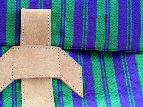 Cream-colored leather strap with stitching detail fastened over vibrant purple and green striped textile background