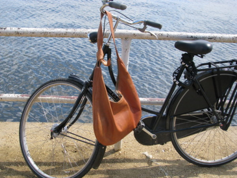 Braune Ledertasche aus Leder hängend an Fahrradrahmen neben Wasser, Vorderansicht