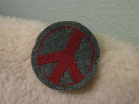 Round grey felt brooch with red cross design, front view on light textured surface