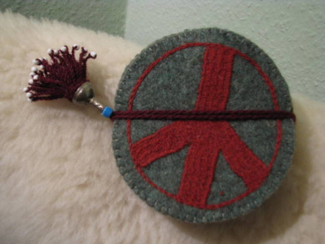Grey felt round pouch with red peace symbol and matching tassel, front view on white fur surface