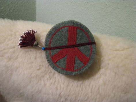 Grey felt coaster with red geometric cross pattern and burgundy pom-pom accent, flat lay view
