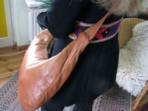 Artisan tenant un sac en cuir marron clair, vue de détail montrant la texture et la patine du cuir travaillé à la main