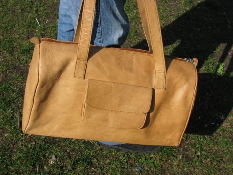 Sac à main en cuir marron clair, forme rectangulaire avec poignées, vue de face sur herbe verte