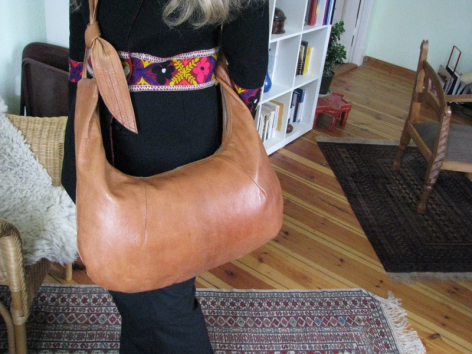 Sac à main en cuir cognac avec détail textile coloré, vue de face tenu par une personne portant un vêtement noir