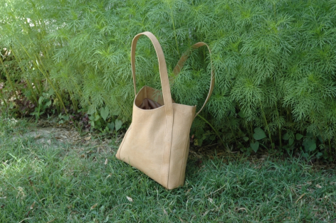 Sac à main en cuir beige clair avec anses longues, posé sur l'herbe verte, vue de face