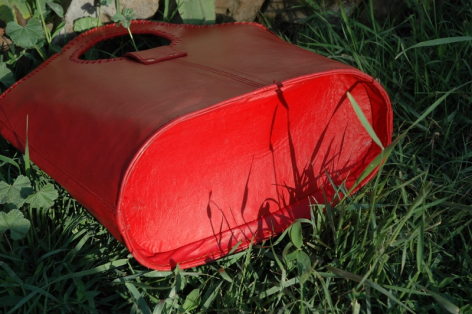 Sac à dos rouge vif en tissu technique, forme ergonomique allongée, posé sur herbe verte