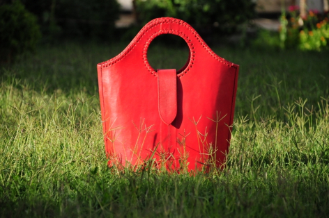 Sac en cuir rouge vif avec poignées, posé sur l'herbe, vue de face