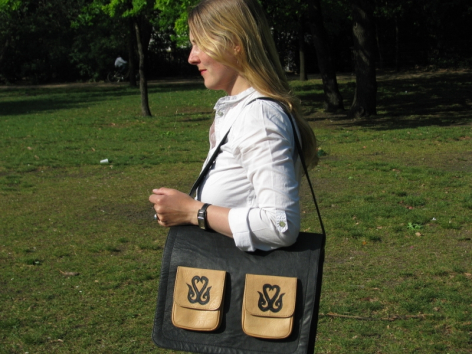 Femme portant un sac en cuir noir avec deux pochettes dorées, vue de profil en extérieur