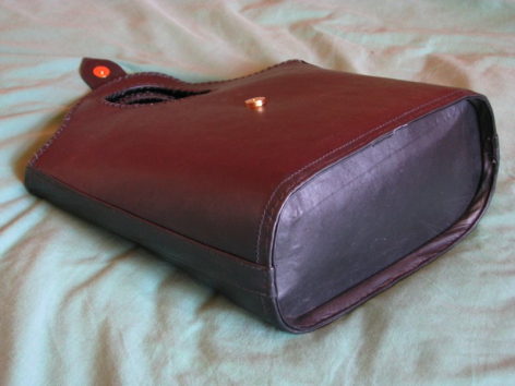 Braune Ledertasche mit abgerundeten Ecken und violettem Farbverlauf, Draufsicht auf beigem Untergrund