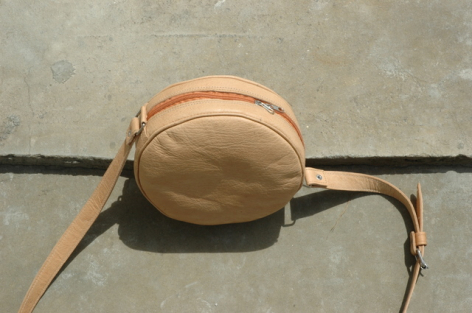 Sac à bandoulière rond en cuir cognac avec lanière noire, vue de dessus sur surface grise
