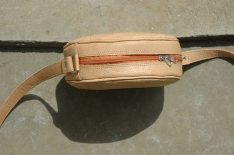 Tan leather waist bag with black adjustable strap, viewed from above showing rectangular shape and front zippered pocket