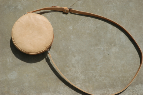 Cream-colored round leather pendant on thin dark brown cord bracelet, front view