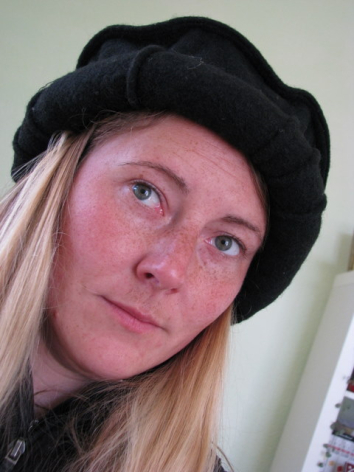 Woman wearing black knit beanie with long blonde hair, looking upward against neutral background