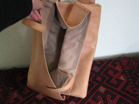 Hellbraune Ledertasche mit rechteckiger Form und geöffnetem Hauptfach, das die Innenseite zeigt, frontal fotografiert