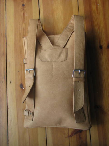 Sac à dos en cuir beige suspendu à un crochet, vue de face montrant les sangles et la fermeture