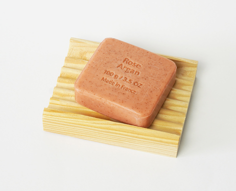 Terracotta soap bar with embossed text resting on a yellow wooden soap dish, top view