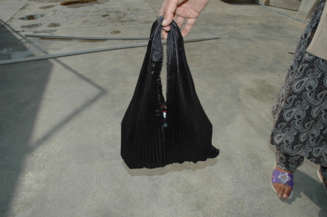 Schwarze Ledertasche mit trapezförmiger Form und langen Henkeln, Frontalansicht auf grauem Untergrund